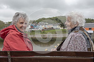 Two senior woman sitting on a park bench outdoors