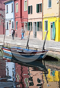 Two Senior woman walking along waterways with traditional colorful facade of Burano and reflection. Venice