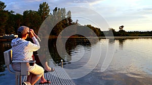 Two senior women on a boat dock bench are watching birds and lake shore scenery.