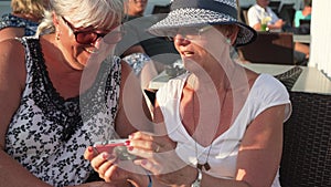 Two senior women in casual summer clothes chatting, watching holiday pictures on their camera during vacation