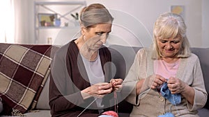 Two senior women knitting sitting nursing home sofa, retirement hobby, relax