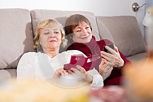 Two senior women with phones on sofa