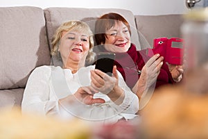 Two senior women with phones on sofa