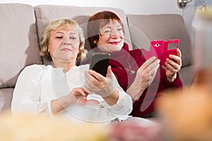 Two senior women with phones on sofa