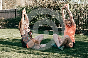 Two senior women in sportswear on grass perform stretching while doing yoga on summer evening