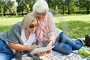 Two Senior Women Using Digital Tablet in Park