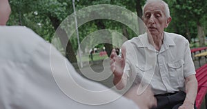 Two seniors friends speaking during playing a chess outdoors and shaking hands