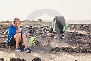 Two seniors and pensioners having a problem in the hiull near to the beach - tired woman waiting to her husband fixing up her bike