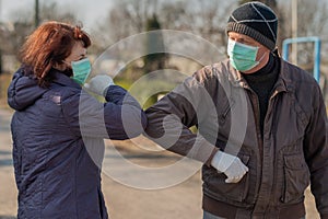 Two seniors wearing facial masks and gloves greeting with elbows