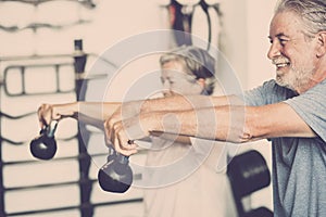 Two seniors working her body to be healthy together at the gym holding a weight - couple of mature people training