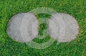 Two separated, rough surfaced, flat, round, concrete tiles in the green grass photo