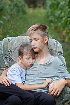 Two serious brothers sitting on a armchair in a field in the countryside in summer day