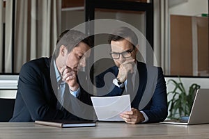 Two serious businessmen, focused business partners, coworkers reading document