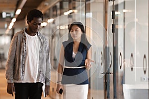 Two serious diverse colleagues talking walking in modern office hallway