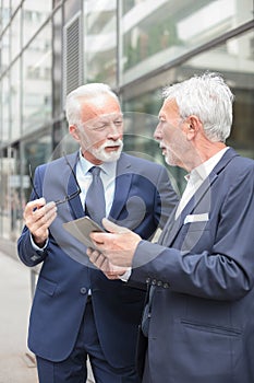 Two serious senior businessmen working on a tablet looking at each other and discussing