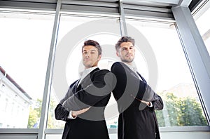 Two serious young businessmen standing with arms crossed in office