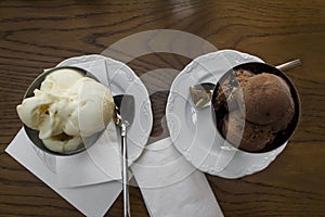 Two servings of ice cream in the stainless steel bowls on the wooden table.T