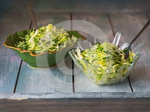 Two servings of malate in different plates on a wooden table. Salad of cabbage, cucumbers and greens