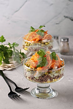 Two servings of salad with Korean carrots, meat and canned peas in transparent salad bowls a light gray background