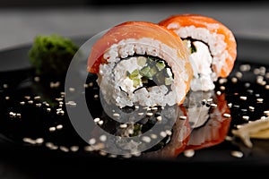 Two servings of sushi with salmon and cucumber with vossabi sauce and ginger on a black plate.