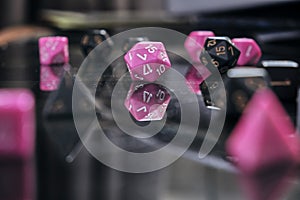 Two sets of role playing game dice, pink and black, on a gaming table. Focus is on the pink 20 sided dice in the center