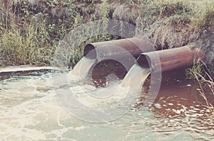 two sewer pipes pour out to the river/Industrial Pipe Dumping Waste Water Into The river. Toned