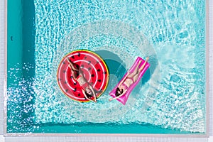 Two sexy girls in bikini are swimming in a pool on inflatable mattresses