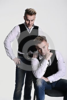 Two sexy twin brothers look at the camera seriously and brutally. on a white background. vests and jeans