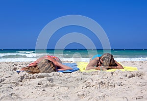 Two young girls laying on a sunny beach on vacation or holi