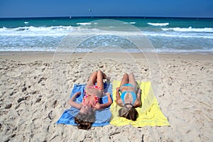 Two young girls laying on a sunny beach on vacation or holi