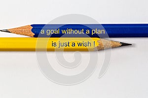 Two sharpened pencils in blue and yellow point in different directions isolated against a white background with the phrase: a goal