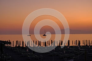 Two ships in the sunset sea, mountains, and sun bed on the beach in Sestri Levante, Liguria, Italy. Summer background