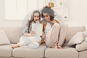 Two shocked female friends using tablet.