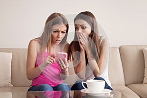 Two shocked young girls looking at smartphone screen.