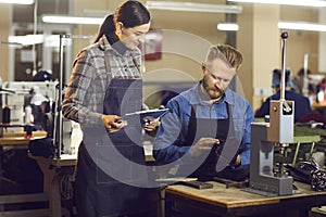 Two shoe factory workers checking the quality of new footwear at manufacturing workshop