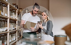 Two shop assistants standing at the counter in zero waste shop, checking stock.