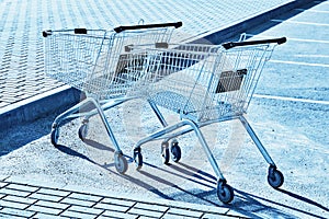 Two Shopping carts in a store parking lot. Blue toning