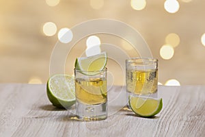 Two shots of tequila with lime slices on a wooden table