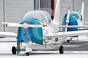 Two shrouded small sports airplanes beside to the hangars