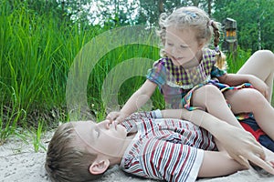 Two sibling children fooling around on white sand dune at pinewood background