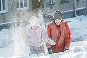 Two sibling children playing outdoors by throwing snow grains in frosty winter sunny day