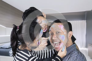 Two sibling doing face painting to their father