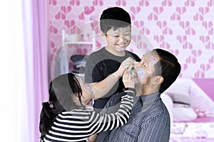 Two sibling doing face painting to their father