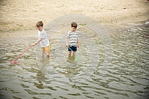 Two sibling little brother boy exploring the beach at low tide walking towards the sea coast. Friendship happy childhood concept