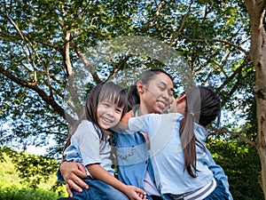 Two sibling little girls with mom laughing and hugging each other on warm and sunny summer day in the garden. Young girls with her