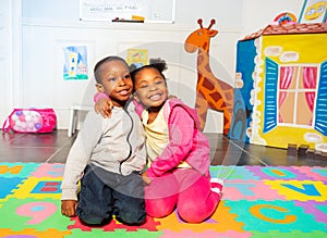 Two siblings boy, girl in play room hug and smile