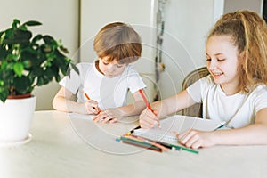 Two siblings brother and sister toddler boy tween girl drawing on table in kitchen at home