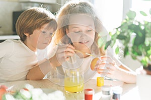 Two siblings brother and sister toddler boy tween girl painting easter eggs on kitchen at home on the spring sunny day