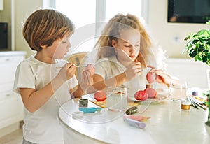 Two siblings brother and sister toddler boy tween girl painting easter eggs on kitchen at home on the spring sunny day