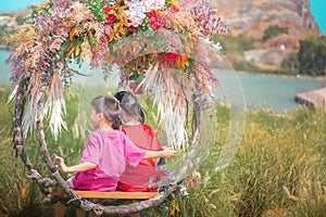 Two siblings children is swinging on a flower swing in a nature field for relaxation and childhood hapiness concept